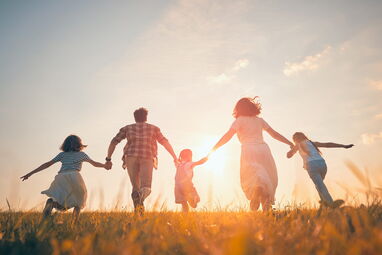 Familie mit zwei Kindern läuft über eine Wiese in der Abendsonne – Urlaub mit Kindern auf Usedom.